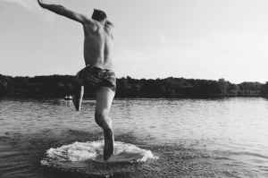 grayscale photography of man jumping on body of water